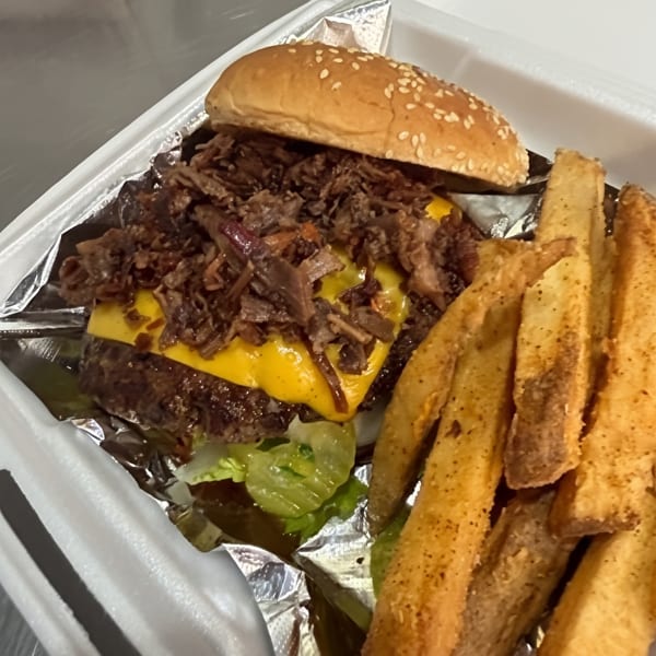 Cheeseburger topped with shredded meat and lettuce, served with seasoned tortilla chips in a foil-lined takeout container.